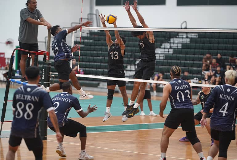 Referee on the left, shot of player spiking volleyball to opposers who are trying to block